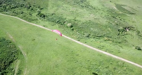 Aerial View of Paraglider Flying Over Green Hills