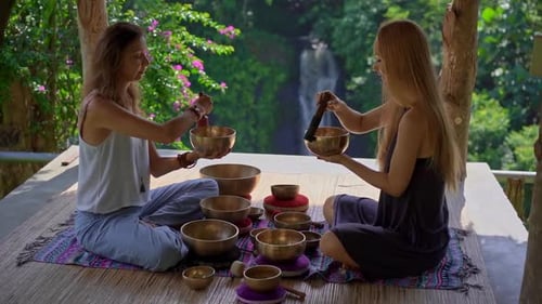 Women Meditating with Singing Bowls near Jungle Waterfall