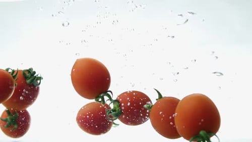 Nahaufnahme von frischen und gesunden Kirschtomaten, die in klares Wasser fallen, mit großem Spritzer auf Weiß