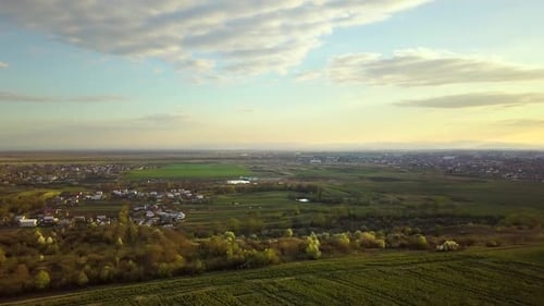 Luftaufnahme von frischen Gartenbäumen, gepflügten Ackerfeldern und entfernten Stadthäusern im Frühling.