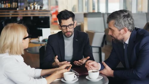 Handsome Entrepreneur Talking To Successful Business People in Modern Cafe