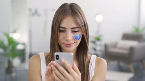 Close-up Portrait of Young Pleasant Woman Texting on Her Phone Sitting at Home