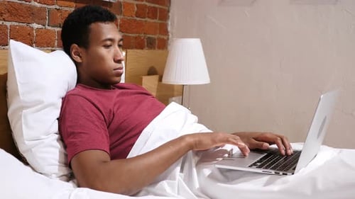 Young Adult Using Laptop Computer in Bed