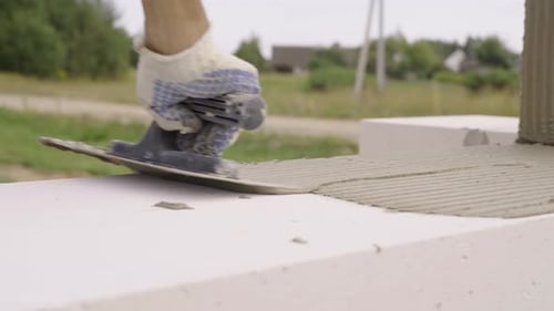 Builder trägt Klebstoffzusammensetzung oder Lösung mit Spachtel auf, um den nächsten Block zu setzen
