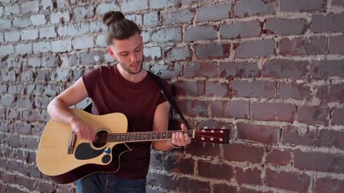 Young Adult Plays Guitar Against Brick Wall