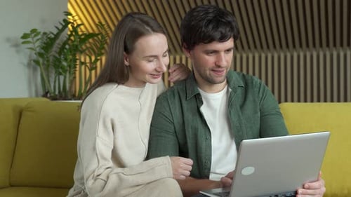 Couple Using Laptop Together on Yellow Couch at Home