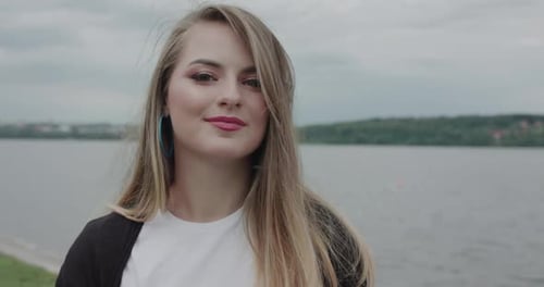 Cheerful Girl Corrects Her Blowing Hair and Smiles at Camera at Seaside Walk