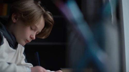 Boy Writes at Desk with Pen Indoors