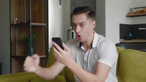 Excited man looking at phone while sitting on couch