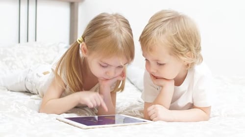 Little Caucasian Kids Use Tablet Sitting on Bed