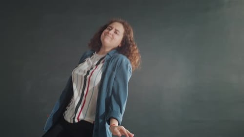 Emotional Girl Dancing in Dark Studio Hall with Grey Wall and Lights in Background