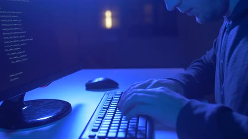 Person Typing on Keyboard in Dark Blue Room