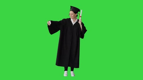 Happy Female Graduate Holding Diploma and Making Selfie on Her Phone on a Green Screen, Chroma Key.