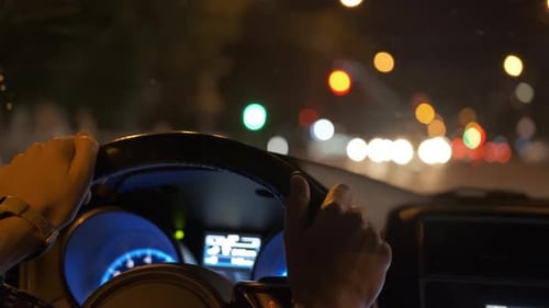 Close Up of Driver Hands Holding Steering Wheel Driving Car with Blurred City Street Lights on