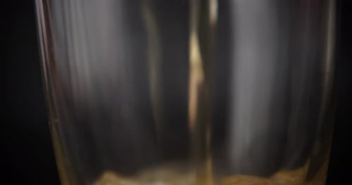 Pouring beer into drinking glass. Dark background, extreme close up, 4K.