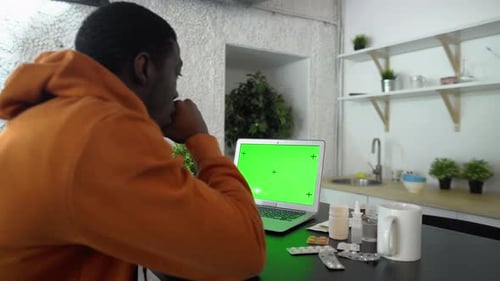 Vista posterior de un joven afroamericano enfermo mira el cuaderno con pantalla verde