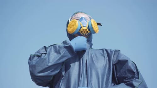 Portrait of Virologist in Biohazard Suit and Respirator Posing at the Background of Blue Clear