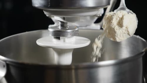 Nahaufnahme des Küchenchefs, der Mehl vom Löffel in eine elektrische Rührschüssel gießt. Zeitlupe. Vorbereitung von