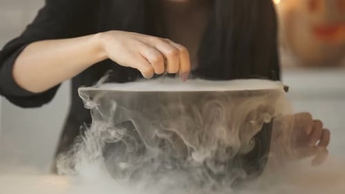 Person Adds Ingredients to Smoky Cauldron