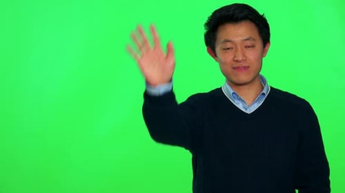 A Young Asian Man Waves and Smiles at the Camera - Green Screen Studio