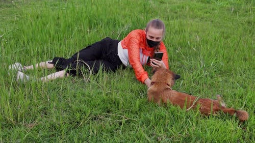 A Young Blonde Woman with a Braid Wearing an Orange Hoodie with a Mask on Her Face Plays on the