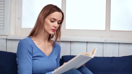 Woman Reading a Book on a Sofa Indoors