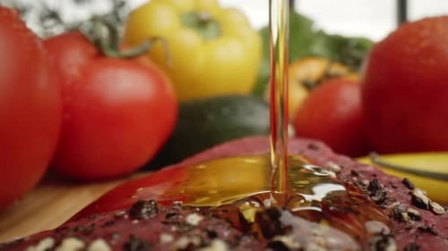Pouring Olive Oil onto Seasoned Steak with Vegetables