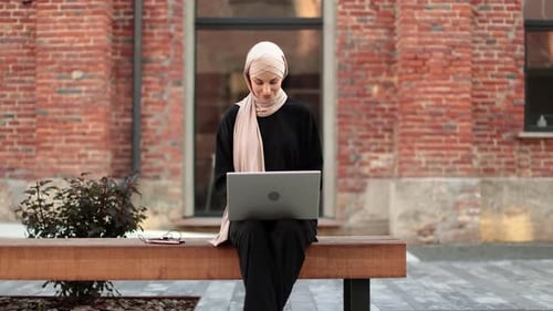 Cheerful Young Islamic Businesswoman Working on Laptop While Sitting Near Her Office