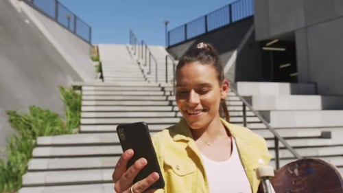 Young Woman with Skateboard Using Smartphone Outdoors
