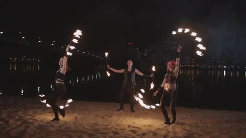 Three Performers Spin Fire Poi on a Beach at Night