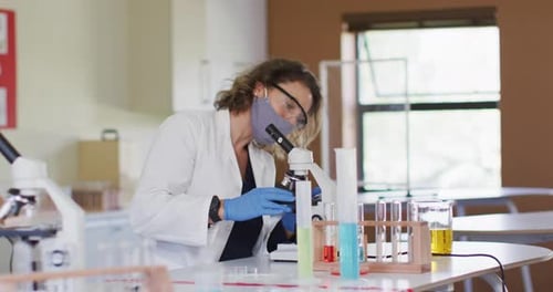 Lehrerin trägt Gesichtsmaske mit Mikroskop im Labor in der Schule