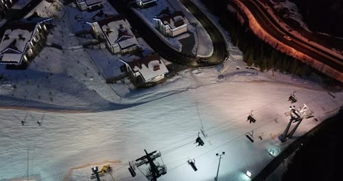 Aerial View of Skiers Go Down Ski Slopes Near Ski Lifts on Ski Resort at Night.