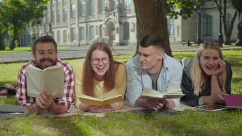 Portrait of Happy Caucasian Male and Female Students Lying with Books on Green Grass and Laughing