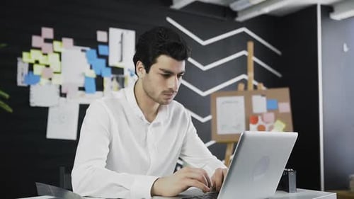 Young Man Works on Laptop in Office Setting