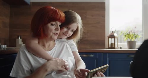 Grandmother and Granddaughter Embrace While Using Phone