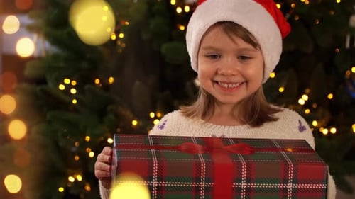 Excited Girl Opening Christmas Gift by Christmas Tree