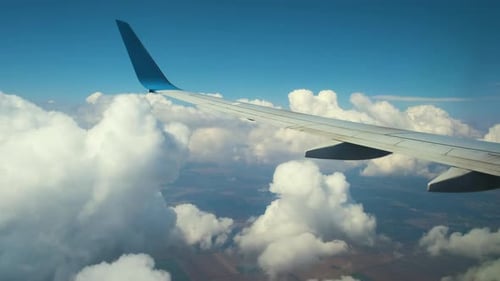 View of jet airplane wing from inside flying through white puffy clouds in blue sky. Travel