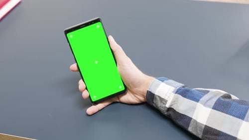 Man Holding a Green Screen Phone on the Table