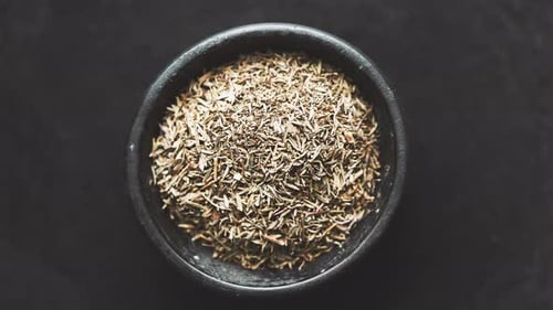 Thym séché dans un bol en bois posé sur une table noire