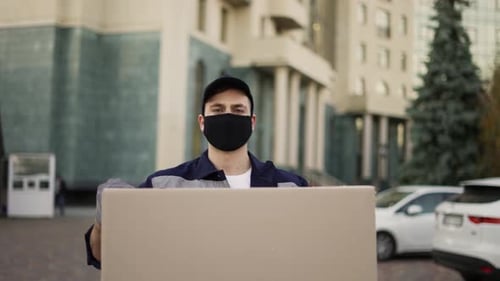 Handsome Delivery Man in Uniform Mask and Gloves Caryying Big Cardboard Box Parcel Outdoor