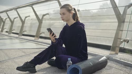 Young Woman Using Phone After Exercise on Walkway