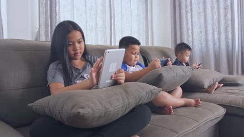 Children Relaxing on Couch While Using Technology