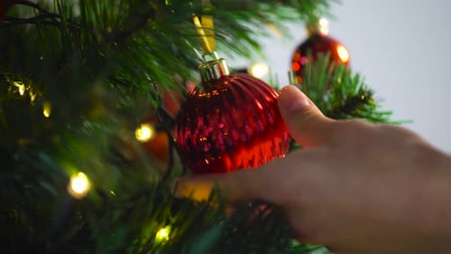 Hand Places Red Ornament on Christmas Tree