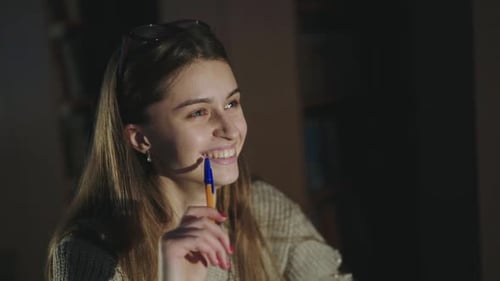 Glückliches Mädchen mit Stift in der Hand Niedliches Lächeln in die Kamera am Schreibtisch in Dim Library
