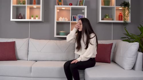 Woman Massages Head on Couch Indoors