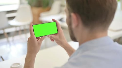 Man Holds Smartphone with Green Screen in Office