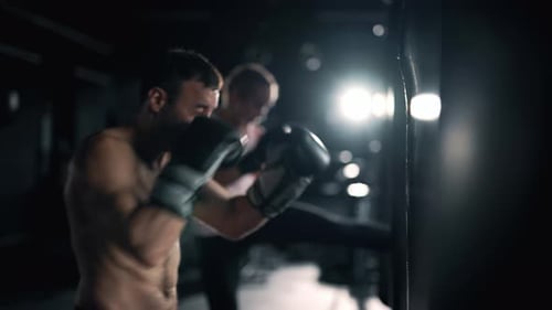 A Muscular Man and Woman are Hits Punching Bag in the Gym