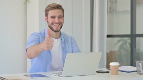 Young Adult Using Laptop Gives Thumbs Up at Desk