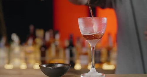 Bartender Pouring Cocktail into Stemmed Glass at Night