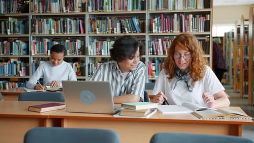 Students Studying in Library Talking Using Laptop Doing Research Together